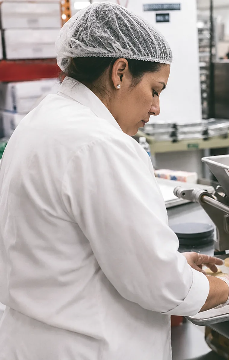 A baker in a commercial kitchen preparing fresh cookie dough on a depositor line.