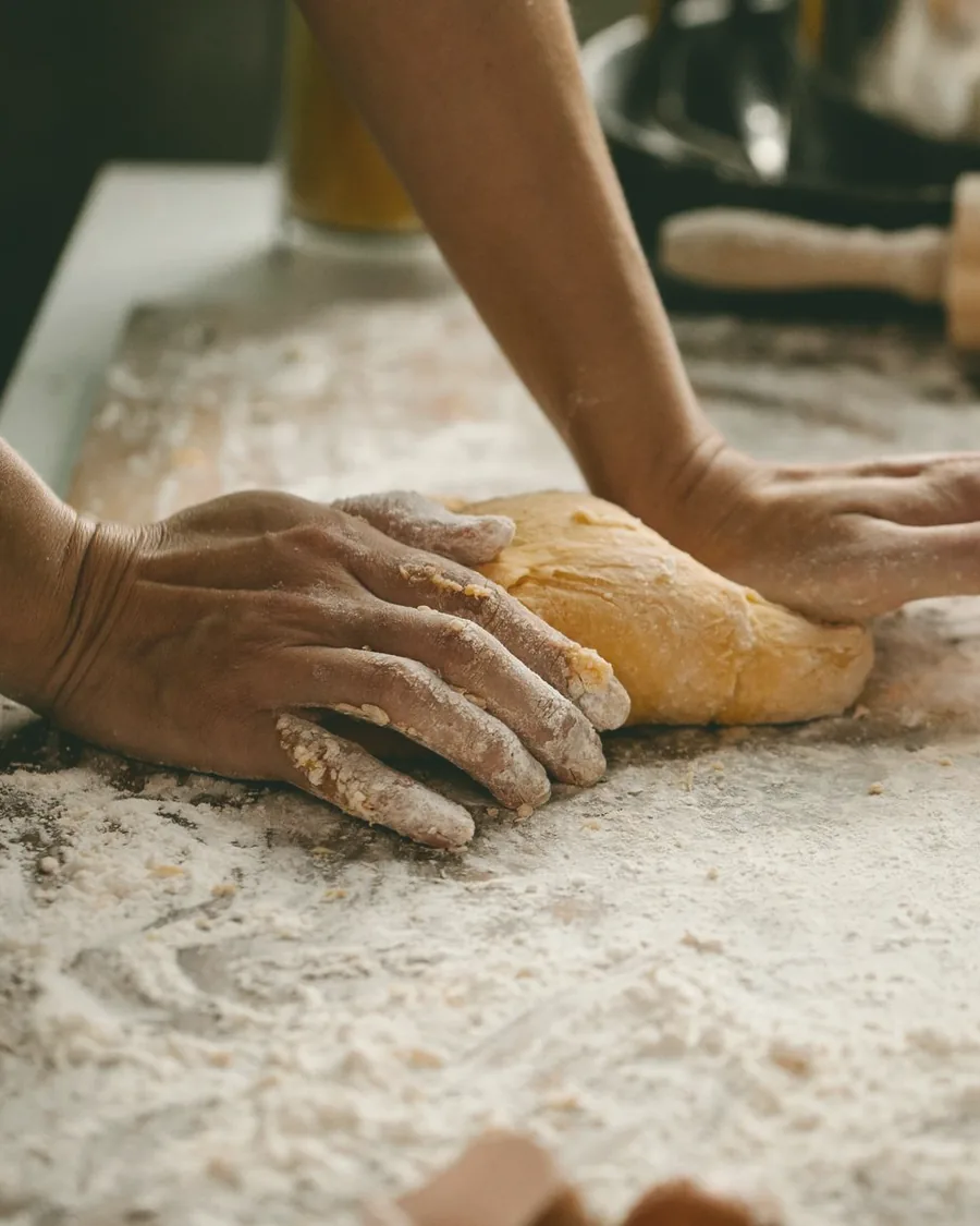 Hands kneading fresh dough on a flour-dusted counter.